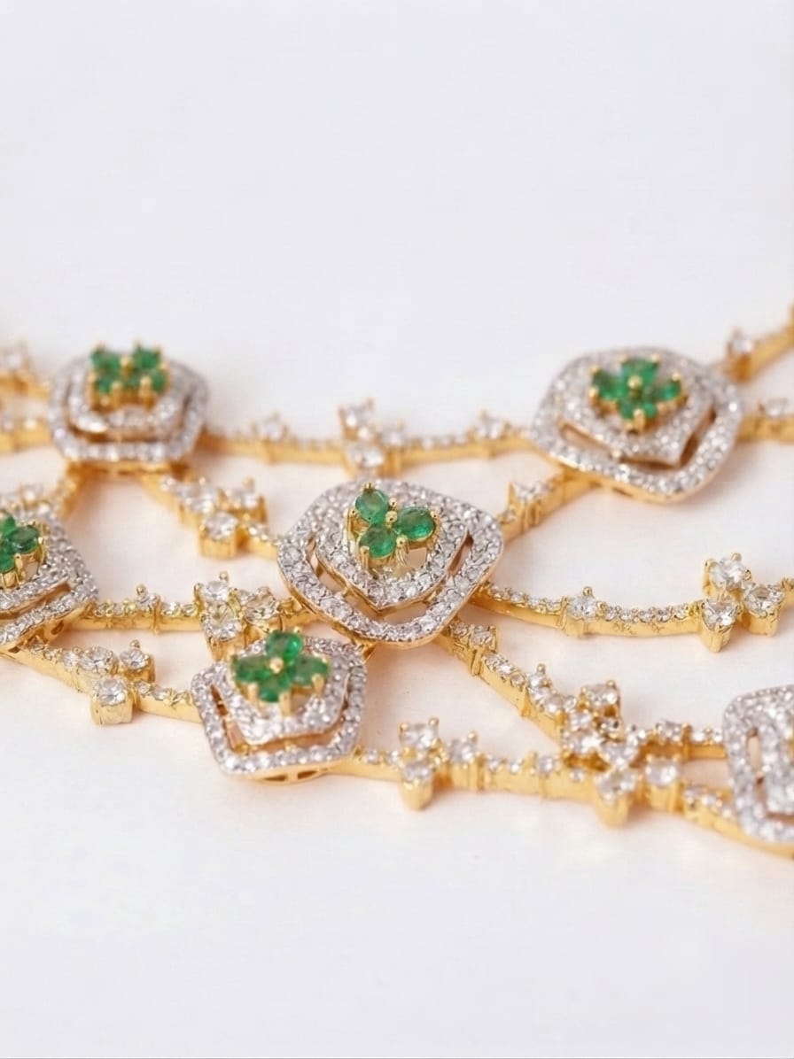 Gold chain jewelry with multiple floral motifs, each featuring a green gemstone center surrounded by clear pavé stones, shown on a plain light background.