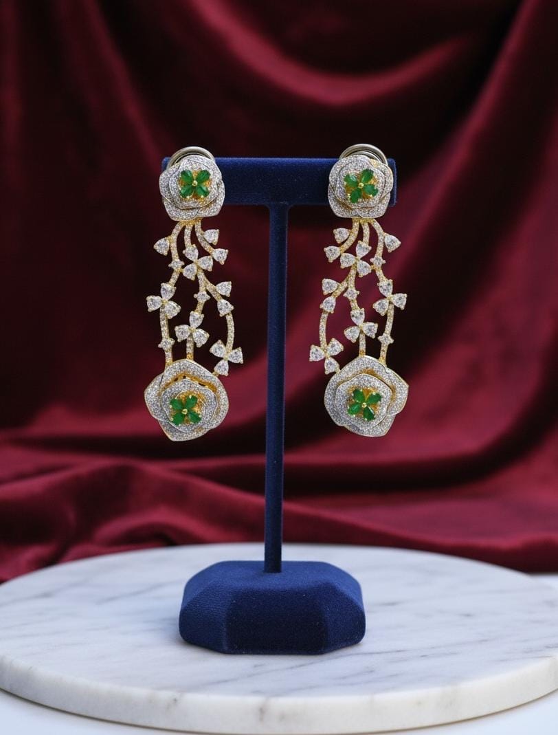 Pair of gold earrings with green gemstones on a blue stand against a red fabric background