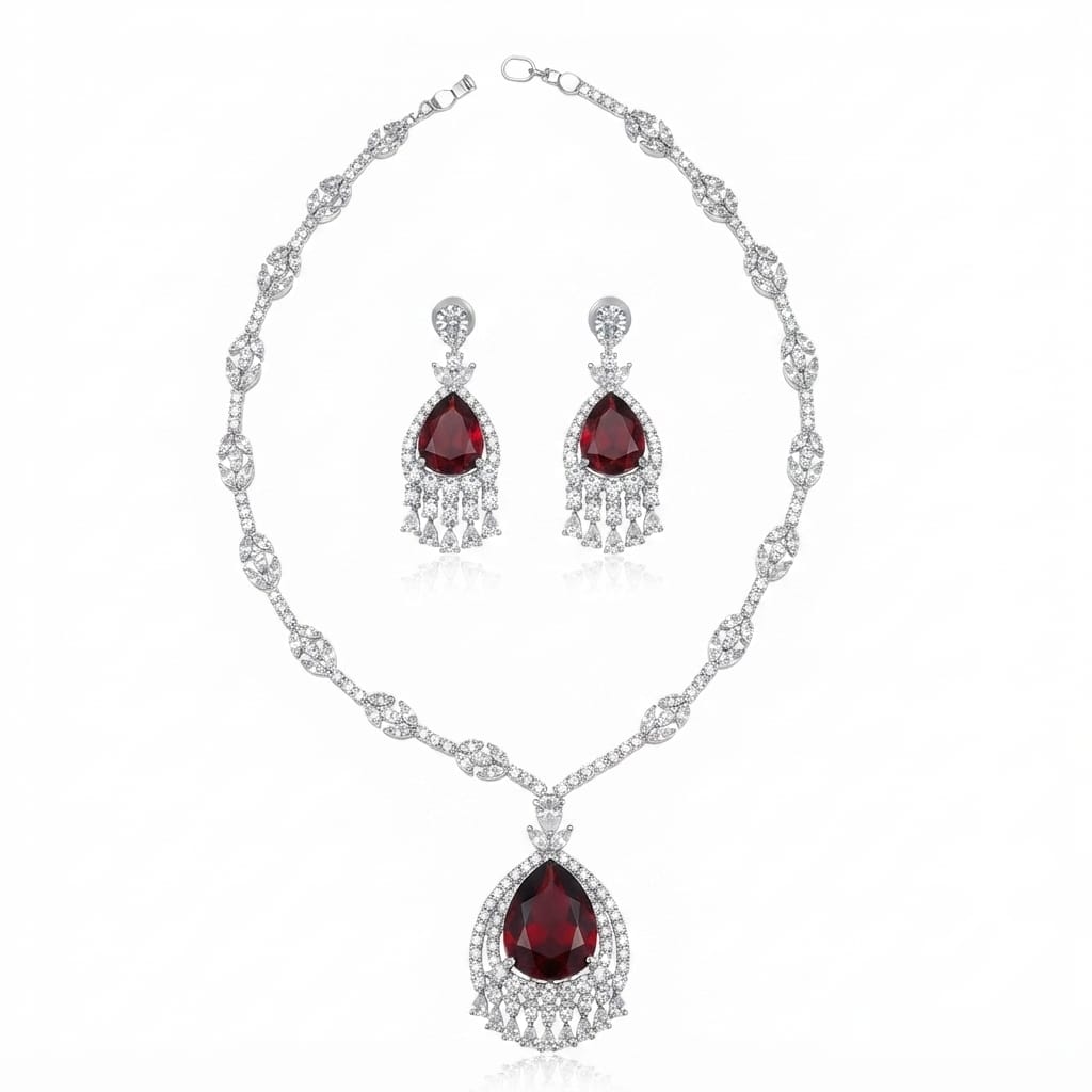 A silver-tone jewelry set featuring a necklace and matching drop earrings, both adorned with clear pavé stones and a teardrop-shaped deep red gemstone at the center.