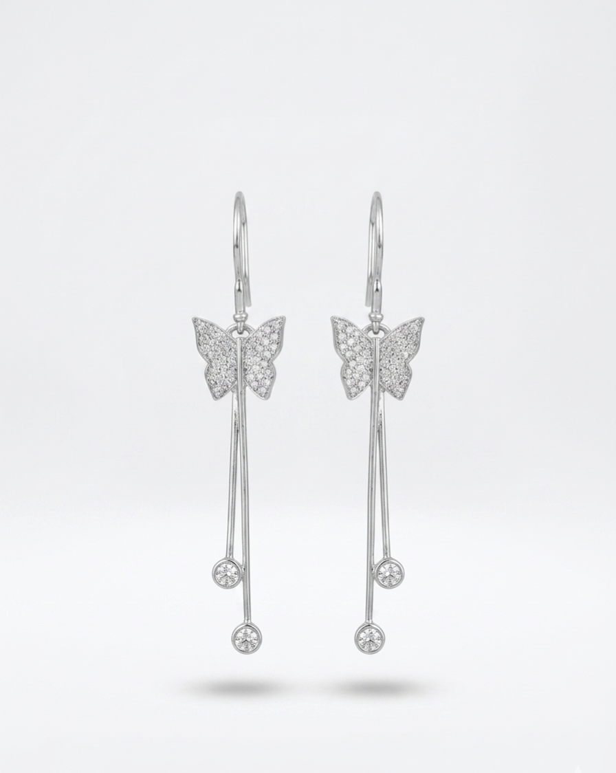 A pair of silver butterfly drop earrings with pavé-set details and dangling bar charms, shown against a light gray studio background.