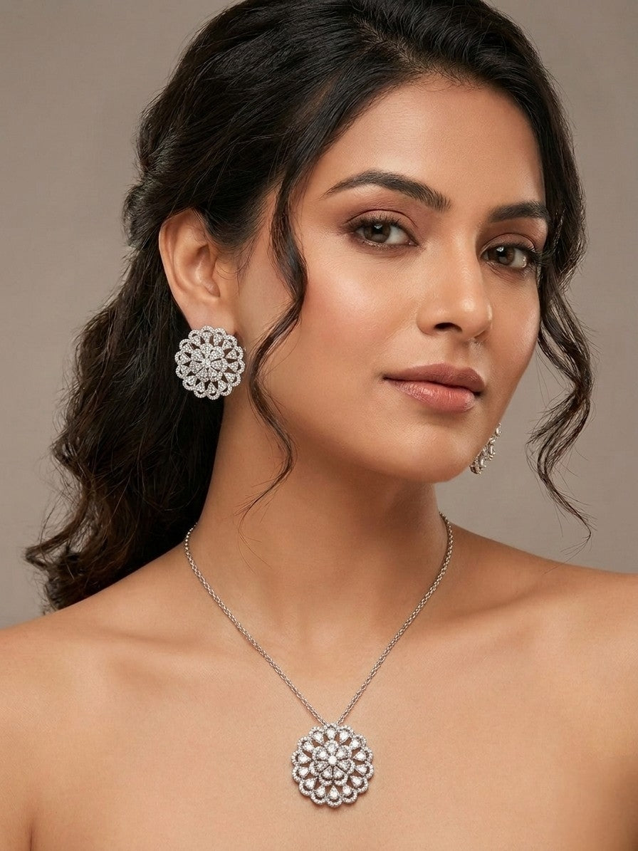 Woman wearing a silver necklace and earrings with green gemstones on a neutral background