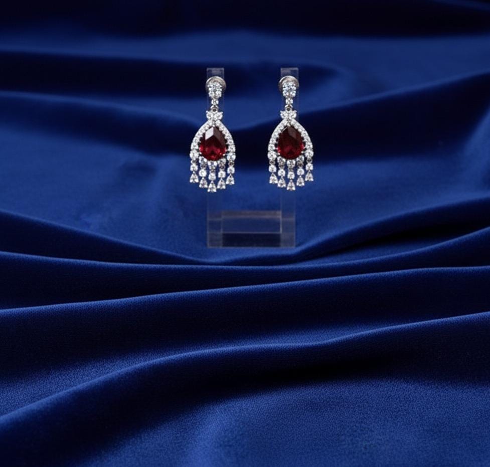 Pair of earrings with red gemstones on a blue fabric background