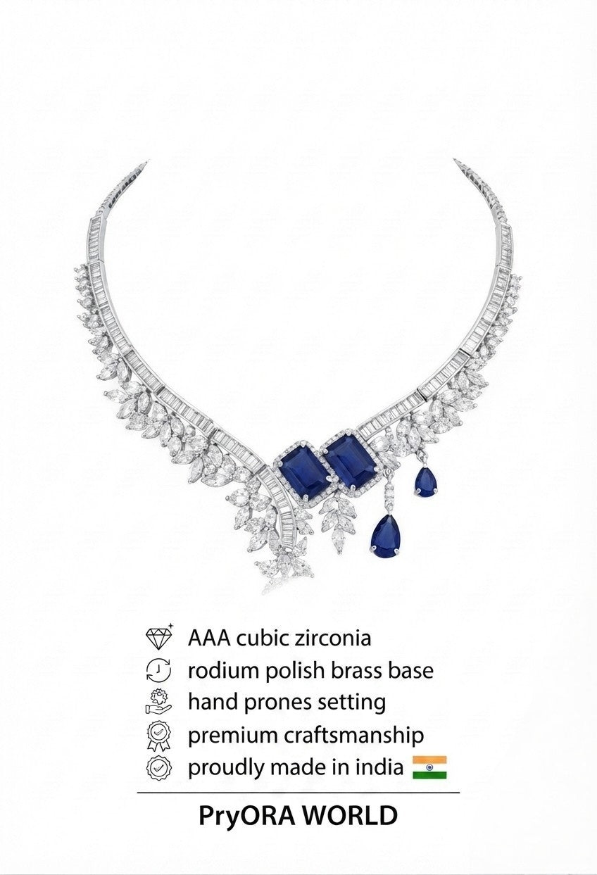 A silver-toned PryorA WORLD necklace featuring rectangular and teardrop-cut deep blue sapphires, surrounded by pavé-set clear stones. The image includes product specifications text below on a plain white background.