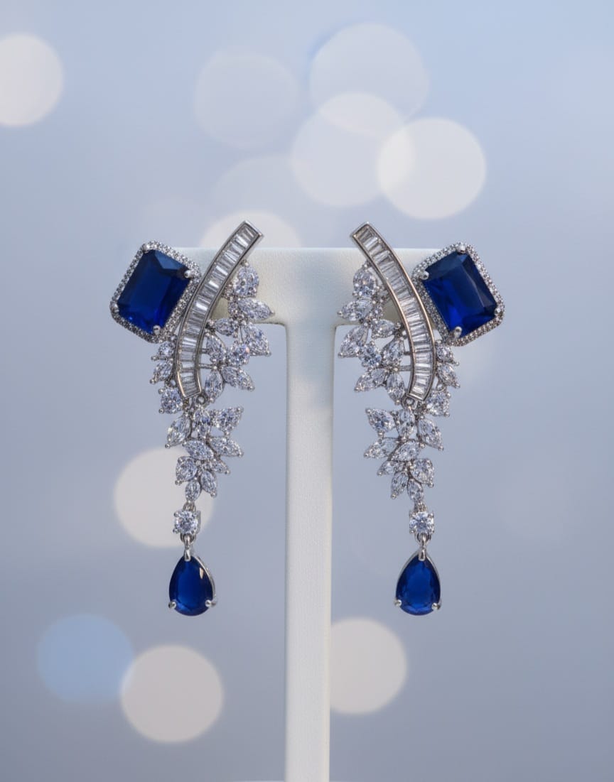 Pair of earrings with blue gemstones and silver accents on a stand against a blurred light background